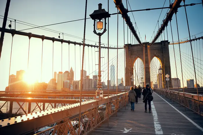 Walk on Brooklyn Bridge with pedestrians at sunset in downtown Manhattan New York City.